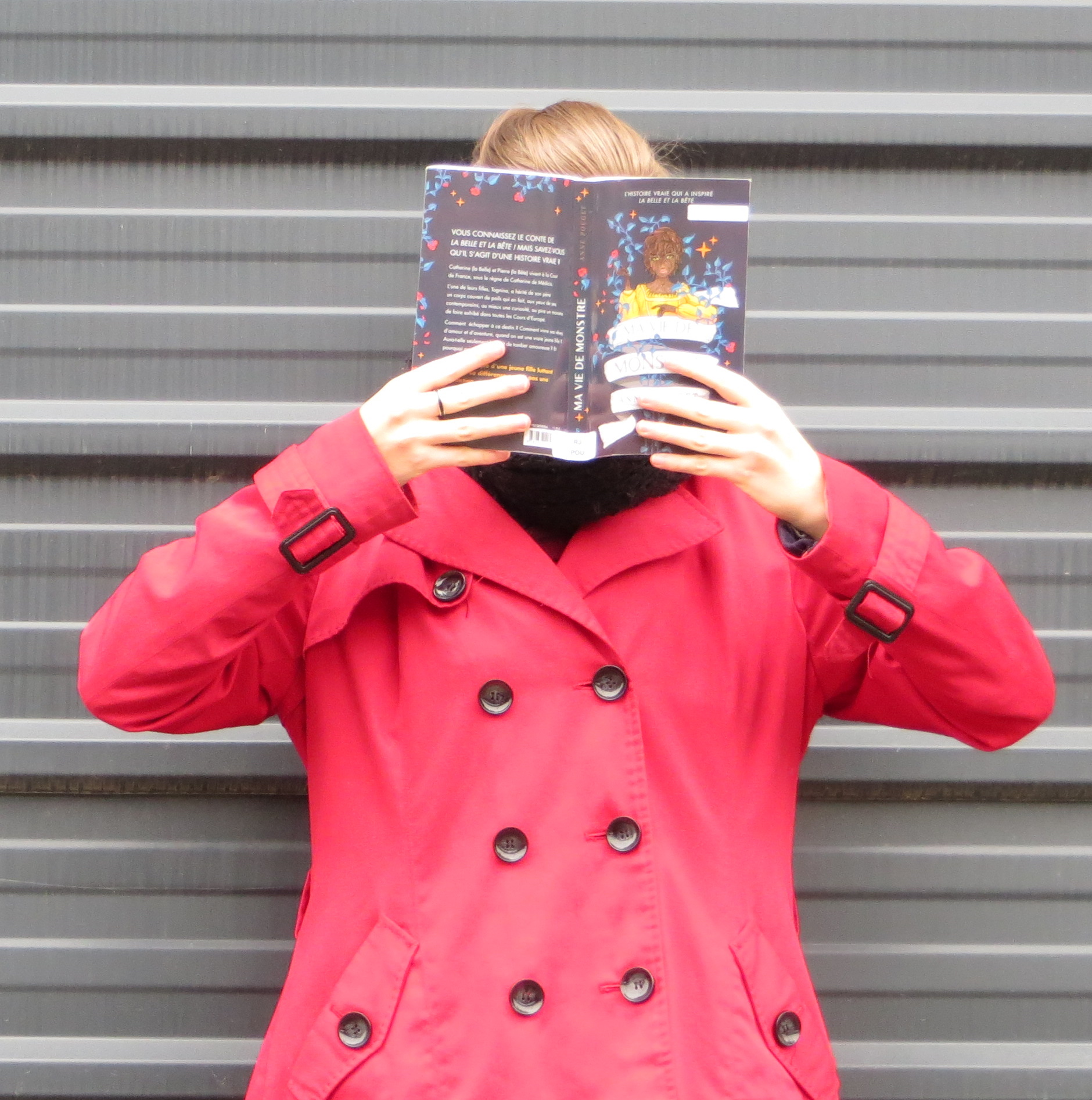 personne en rouge lisant Ma Vie de Monstre d’Anne Pouget devant un mur de métal