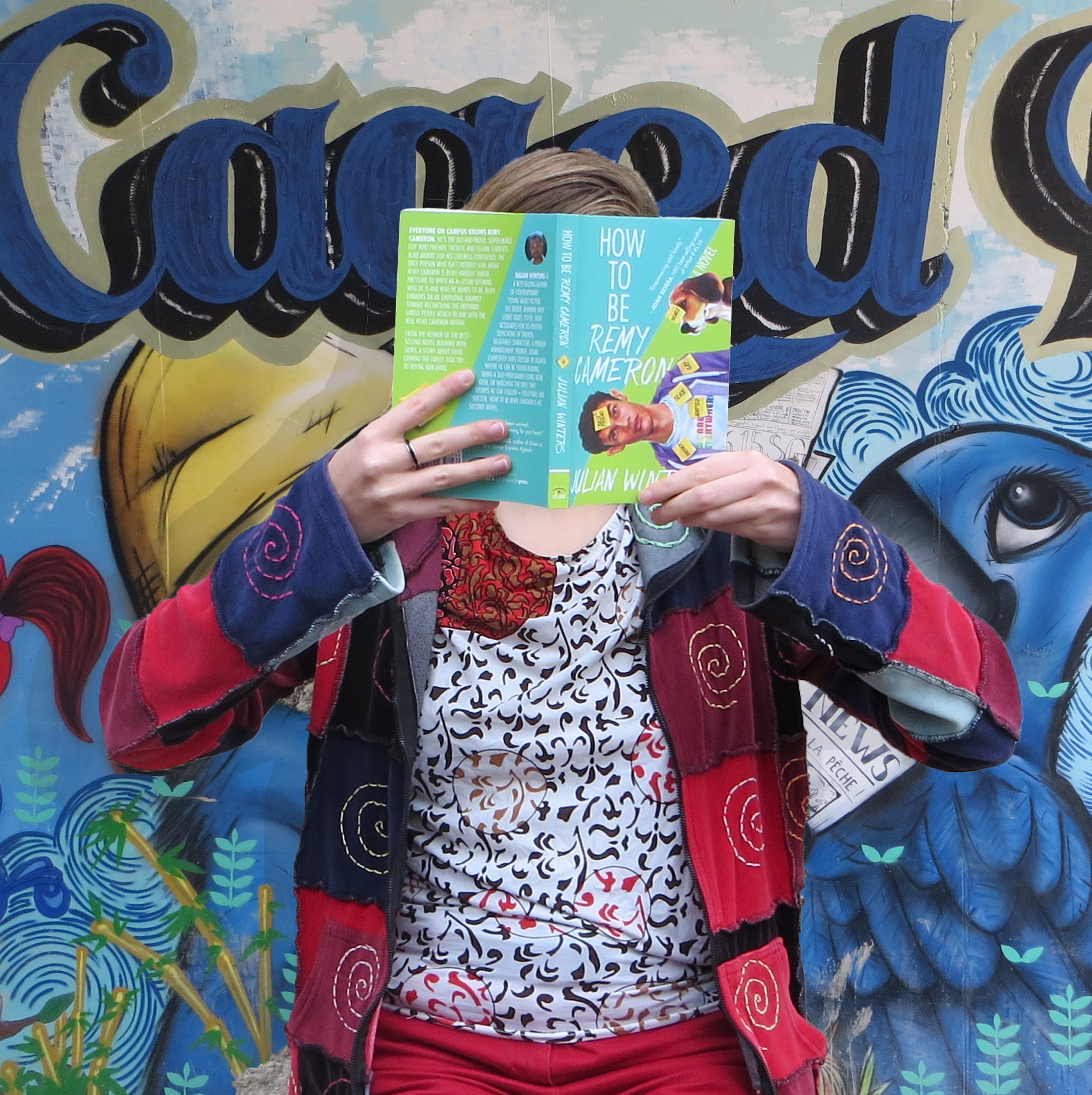 femme en gilet patchwork lisant How to be Remy Cameron de Julian Winters devant un tag avec écrit Caged et les oiseaux du film Rio