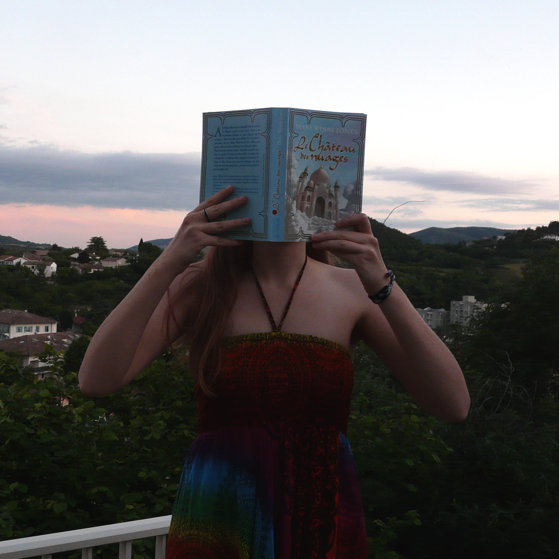 personne en robe multicolore lisant Le Château des nuages de Diana Wynne Jones devant un coucher de soleil