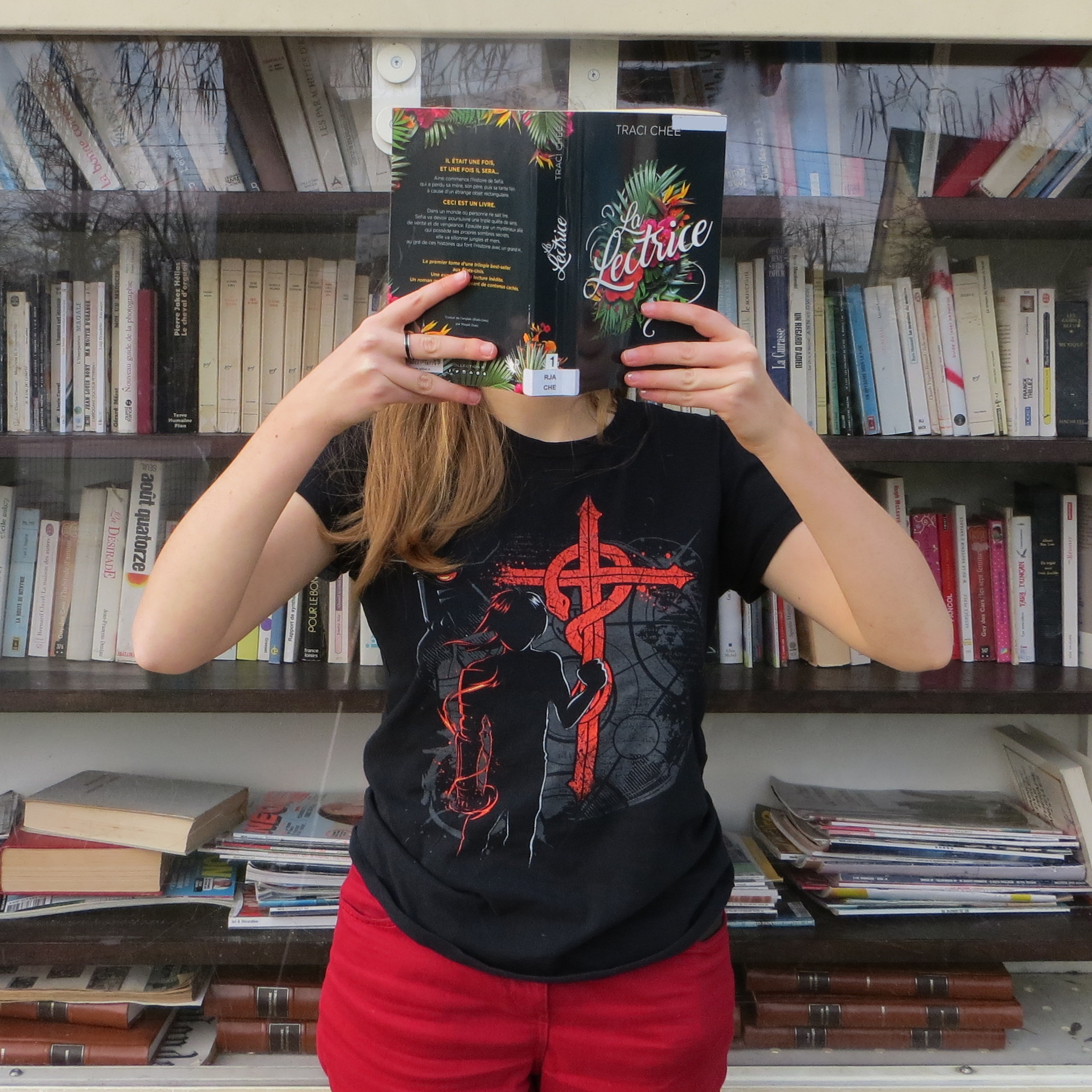 personne en t-shirt fullmetal alchemist lisant La Lectrice devant une bibliothèque