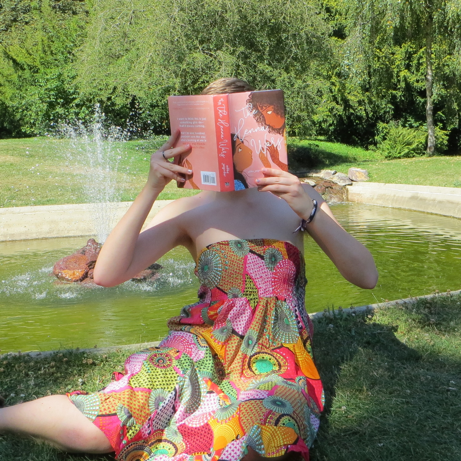 personne en robe multicolore lisant devant une fontaine