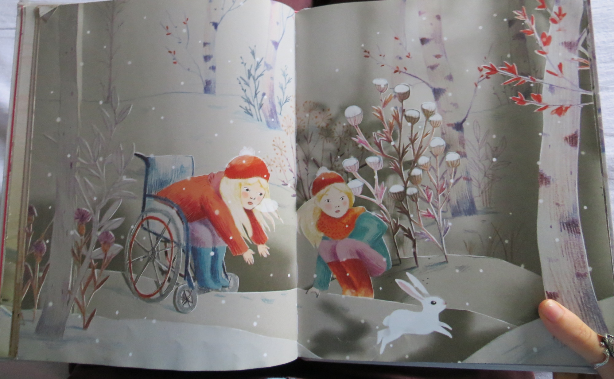 page de Le lapin des neiges de Camille Garoche, on y voit deux jumelles blondes dans la neige, l'une est en fauteuil roulant et un lapin vient de bondir de ses genoux, elles le regardent avec un air étonné et inquiet