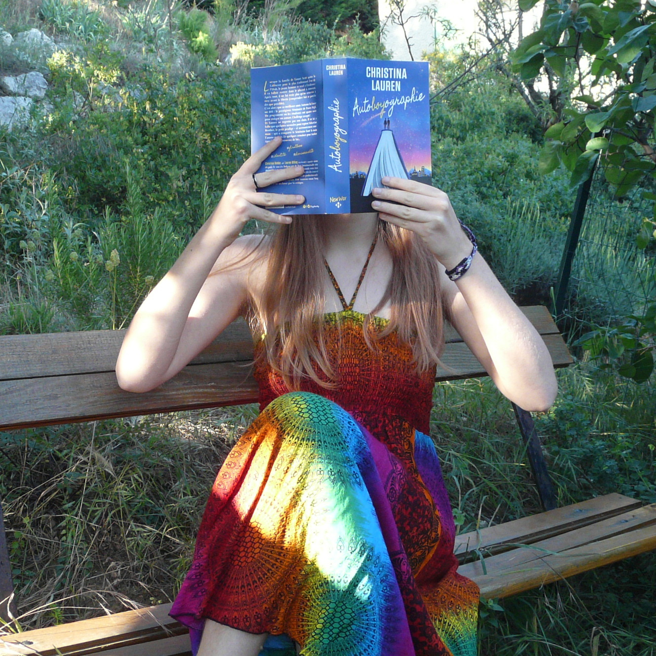 personne en robe multicolore flashy lisant Autoboyographie de Christina Lauren assise sur un banc