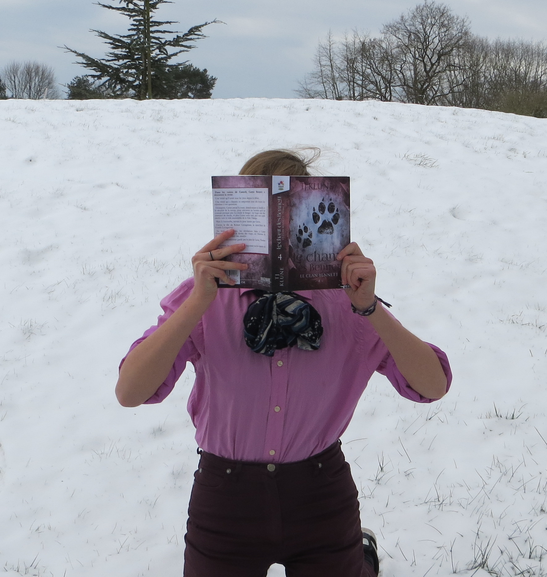 personne en chemise rose lisant Le Chant des Bennett de T.J. Klune dans la neige