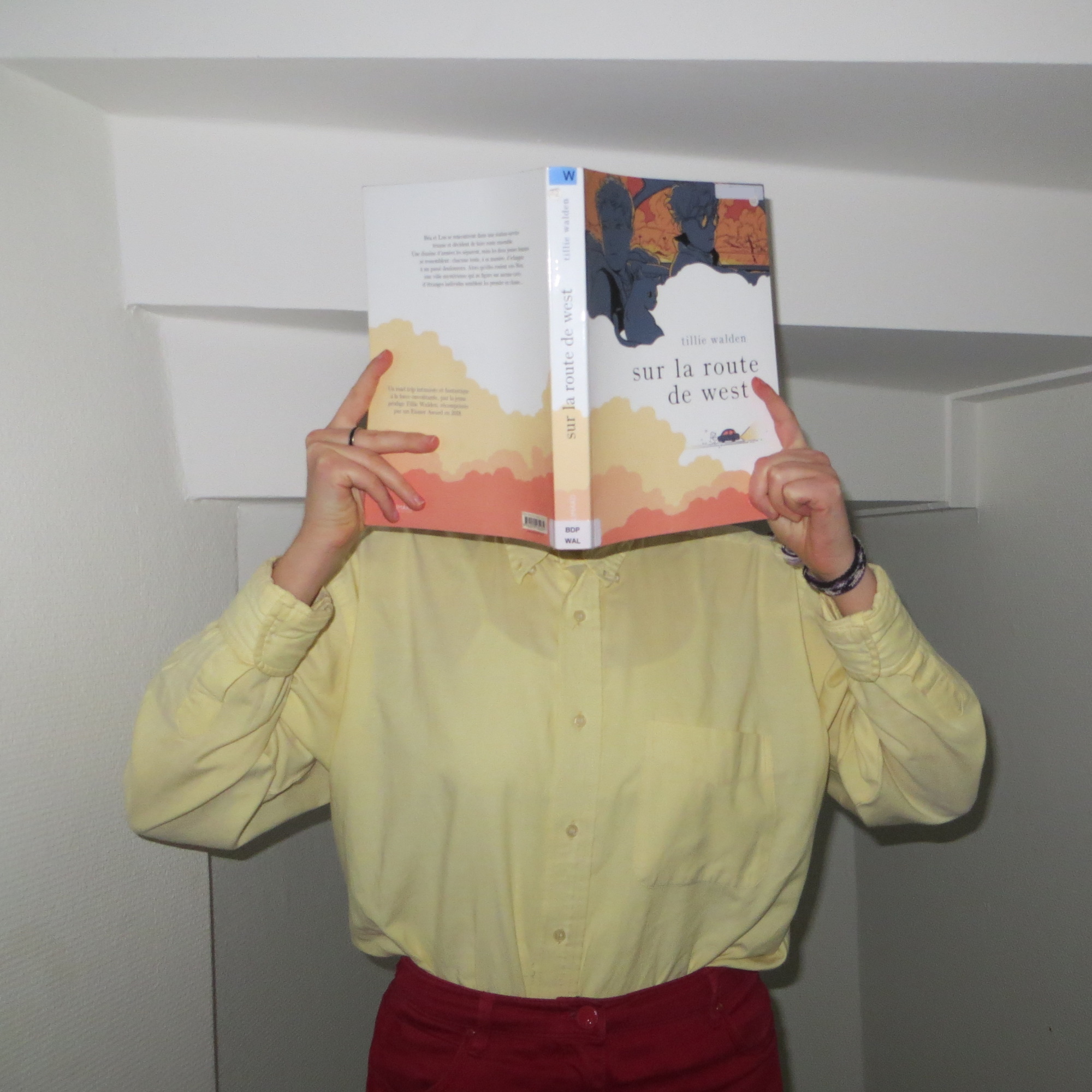 personne en tenue rouge et jaune lisant Sur la Route de West de Tillie Walden dans une cage d'escalier