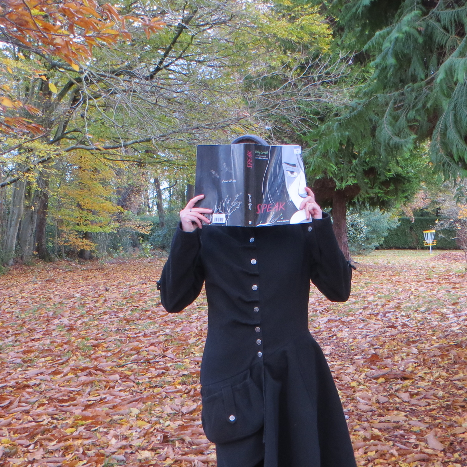 personne en manteau noir lisant Speak de Laurie Halse Anderson & Emily Carroll devant des arbres d'automne