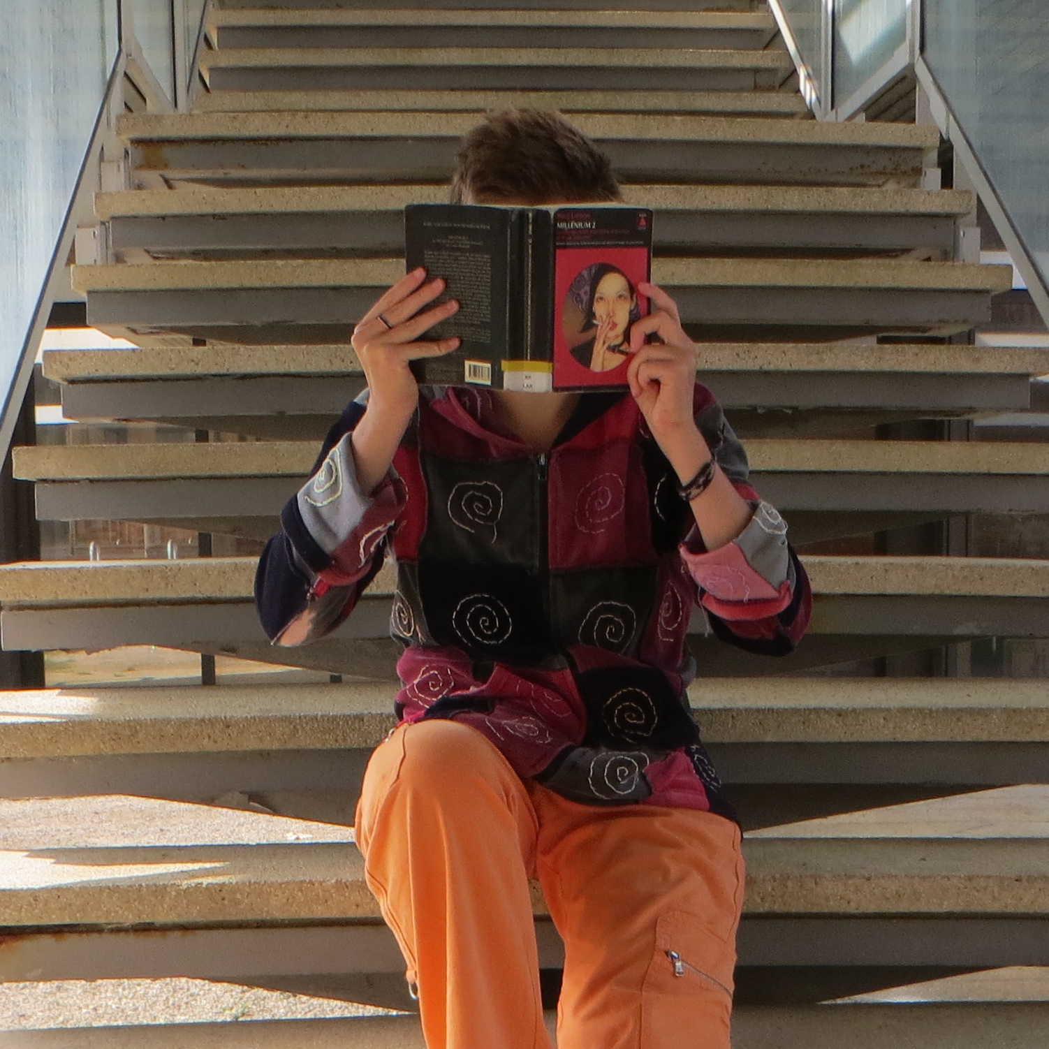 personne en gilet à spirales lisant Millenium 2 : La Fille qui Rêvait d’un Bidon d’Essence et d’une Allumettede Stieg Larsson assise sur des escaliers