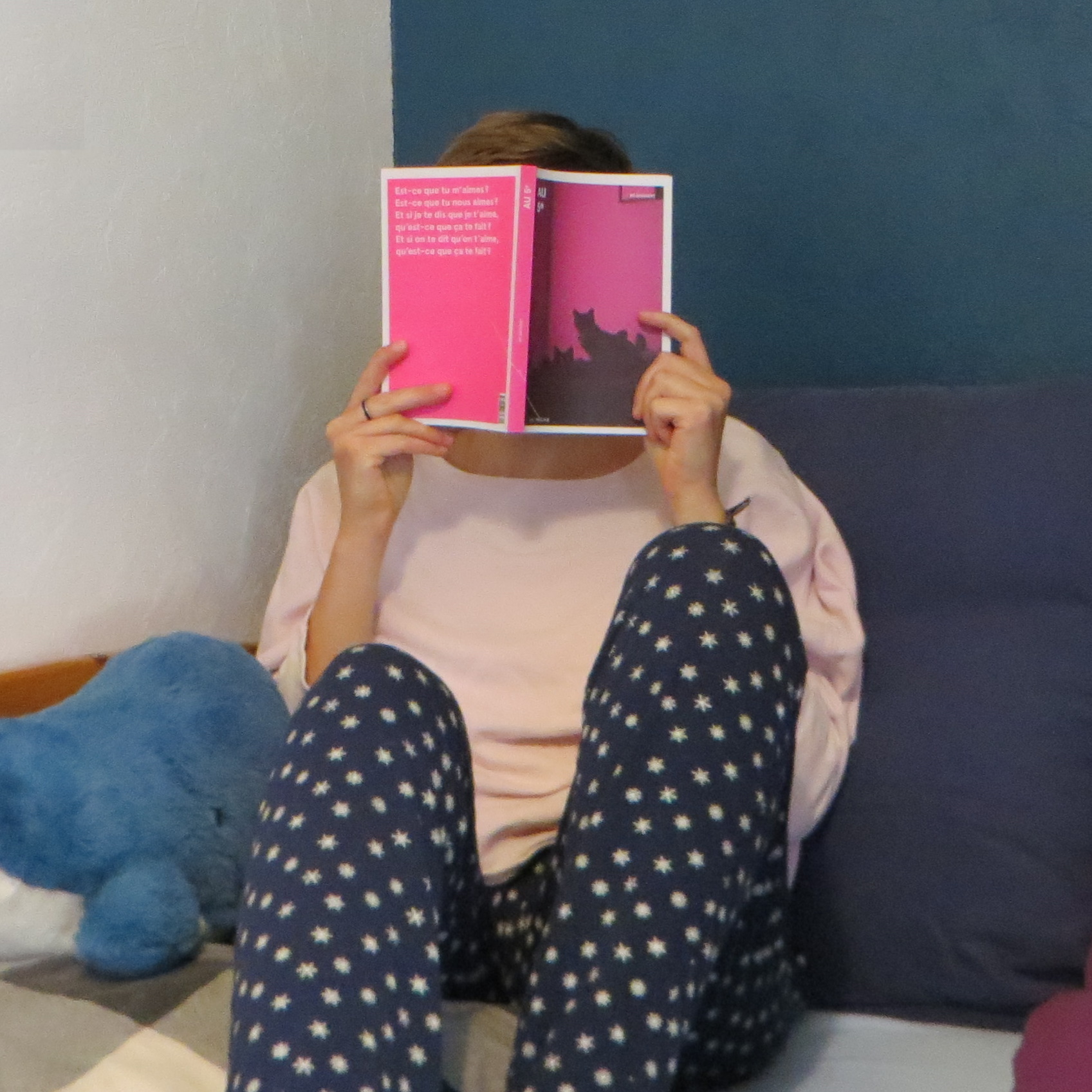 personne en pull rose et pyjama bleu lisant Au 5e de M.P. Boisvert dans un lit avec des coussins bleus