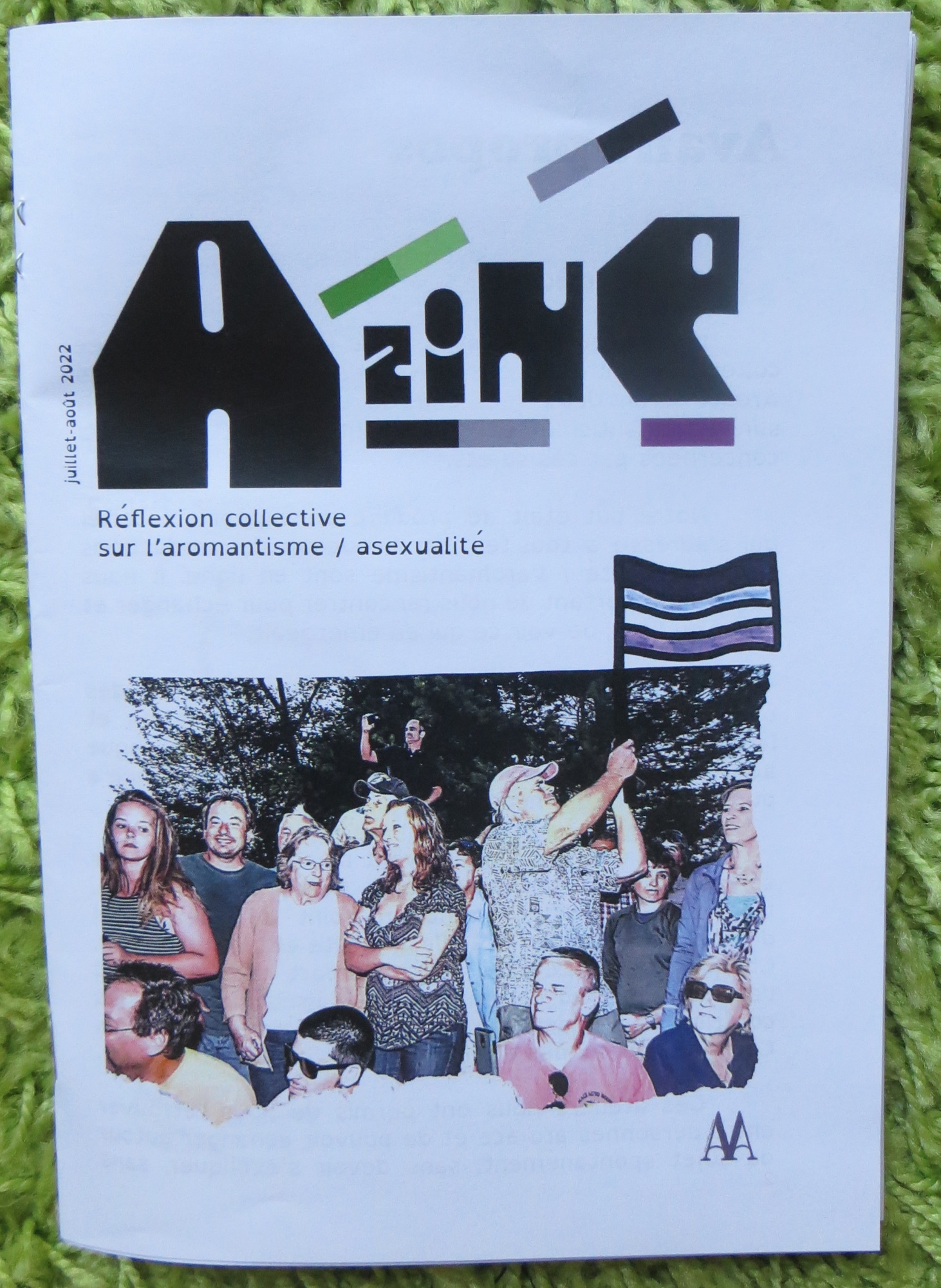 exemplaire du fanzine Azine : Réflexion collective sur l'aromantisme et l'asexualité, illustré par une photo de personnes tenant un drapeau ace, et la date juillet-août 2022