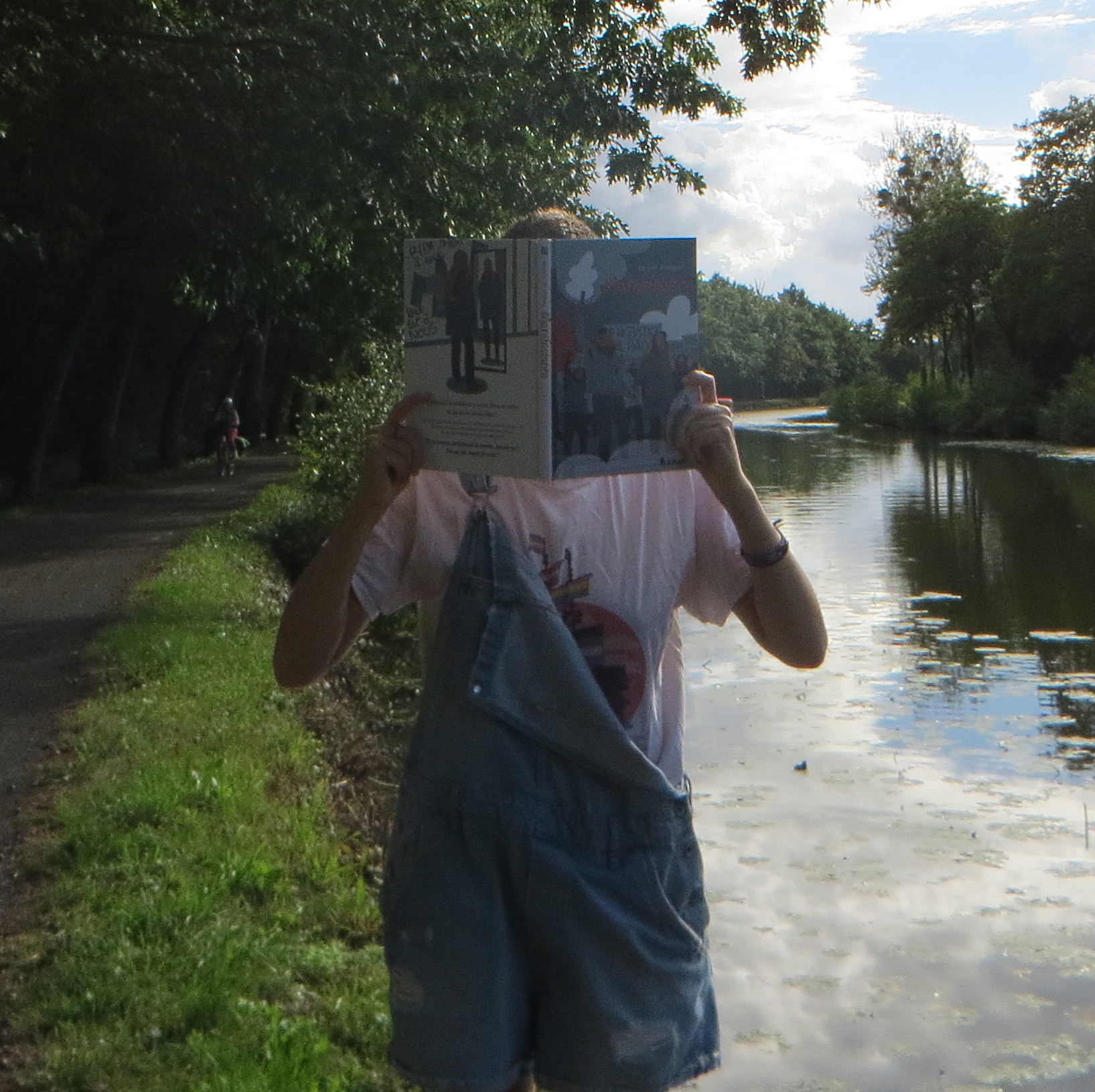 personne en salopette avec t-shirt queer lisant Manifestante d’Hélène Aldeguer devant un fleuve