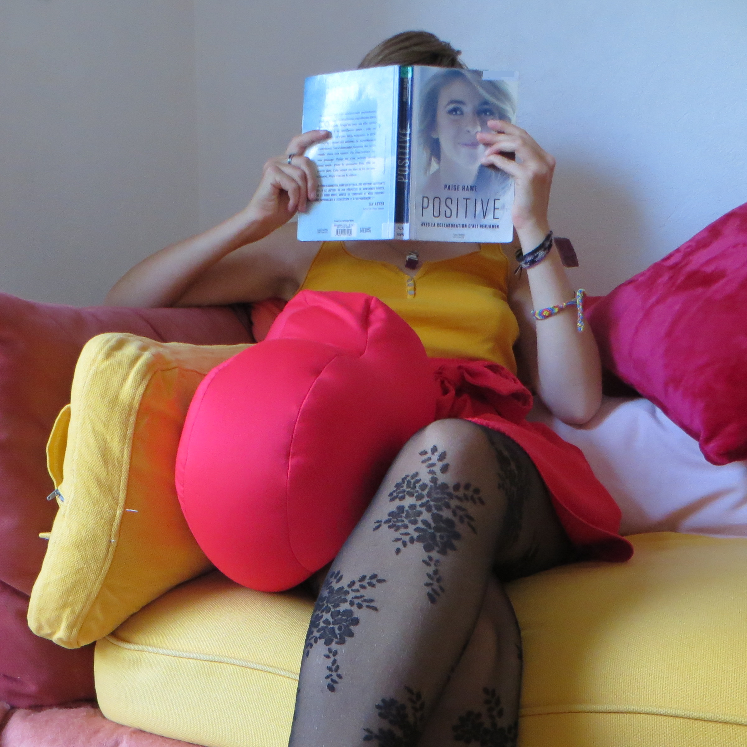 personne en jupe rouge et collants lisant Positive de Paige Rawl sur un coin de canapé jaune