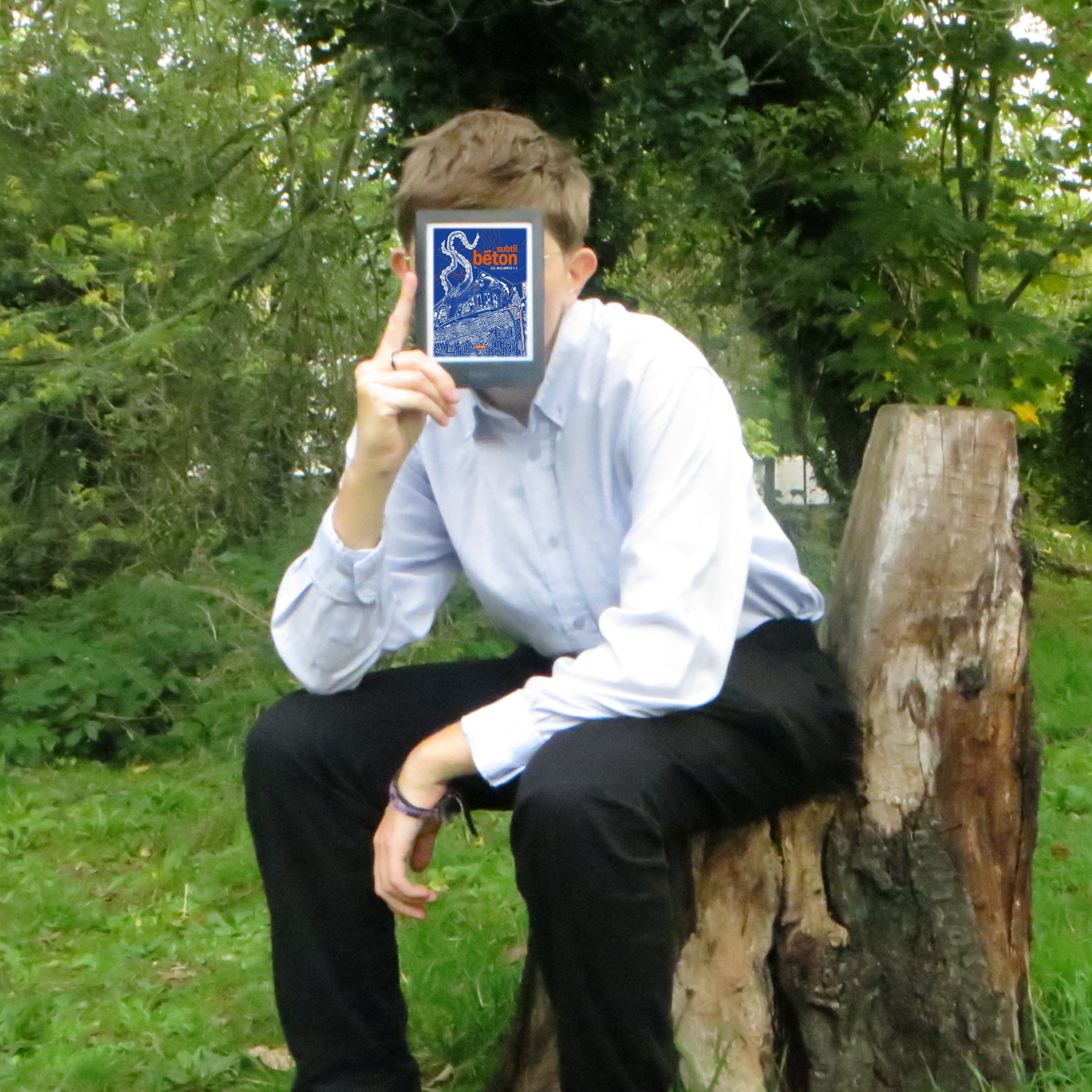 personne en chemise bleue lisant Subtil Béton de Collectif Agloméré·es sur un siège découpé dans un arbre, dans la forêt