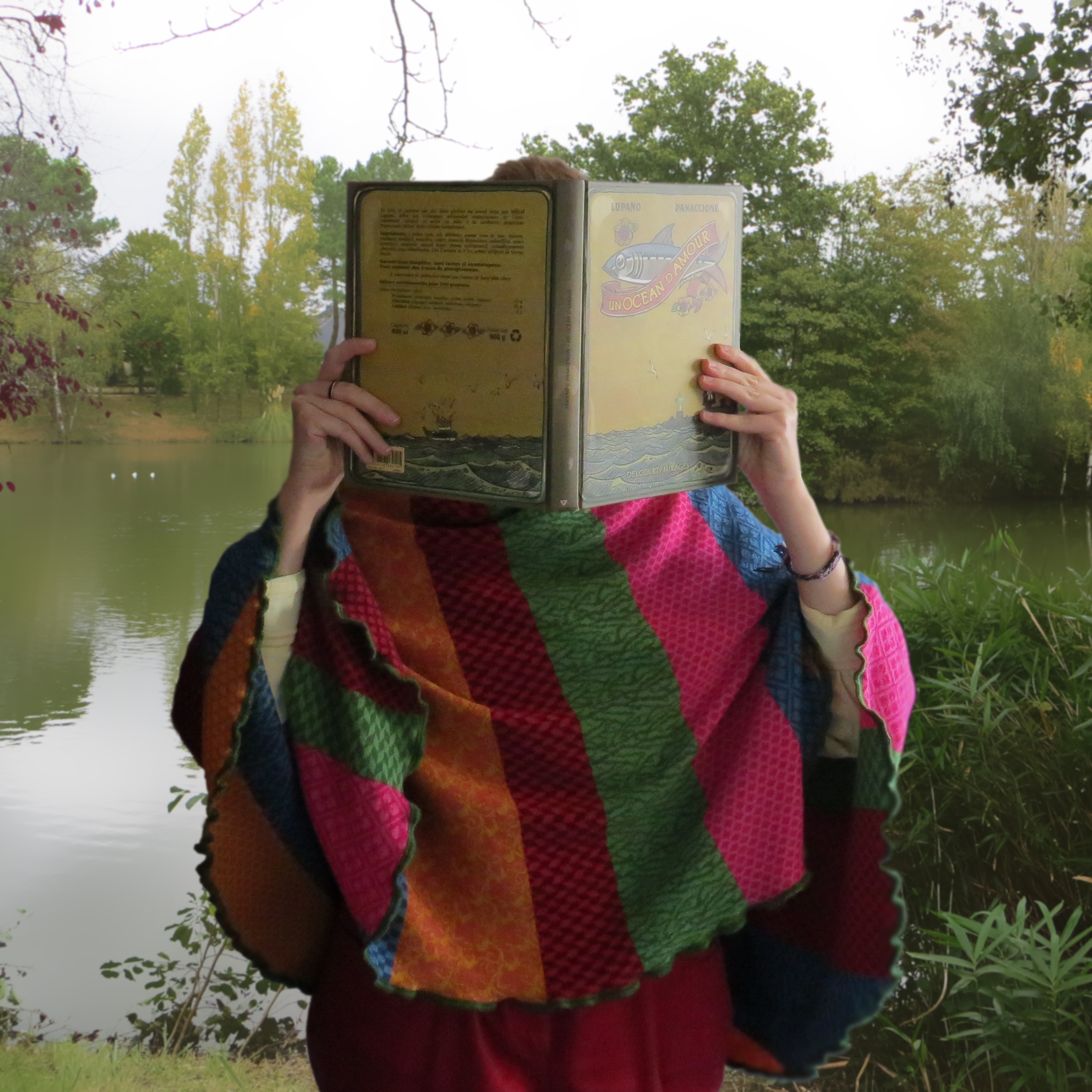 personne en poncho multicolore lisant Un Océan d’Amour de Wilfrid Lupano & Grégory Panaccione devant un lac