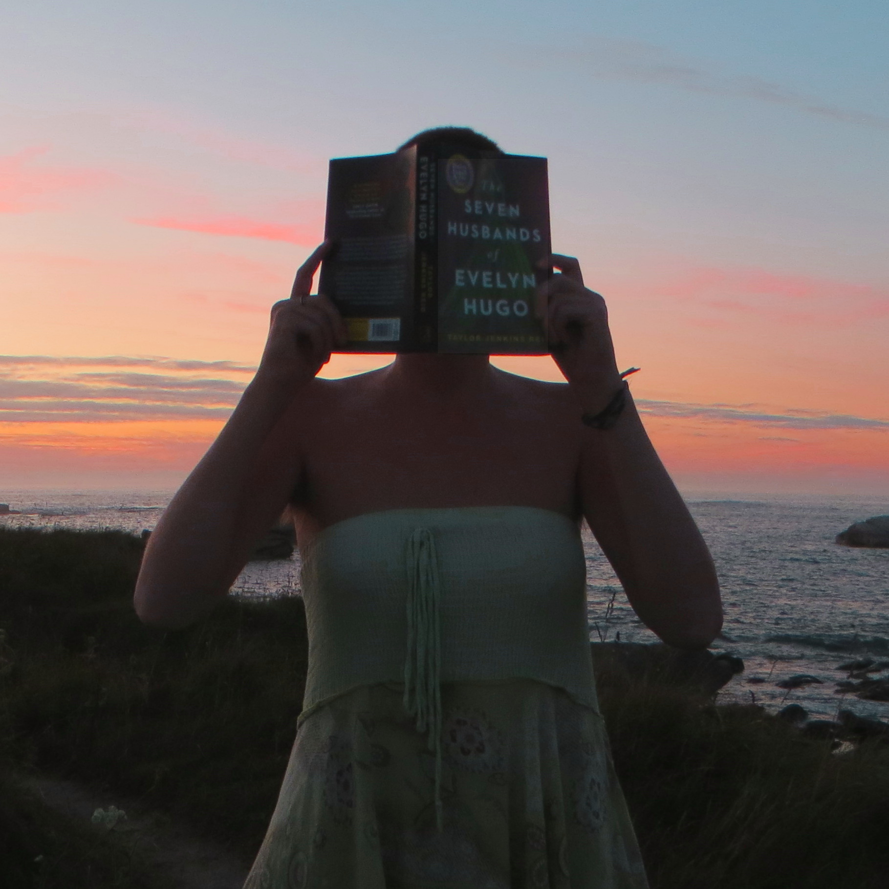 personne en robe verte lisant devant un coucher de soleil sur la mer