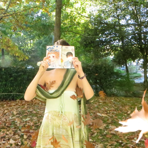 personne en robe verte lisant Josée le tigre et les poissons de Seiko Tanabe & Nao Emoto au milieu de feuilles d'automne qui volent