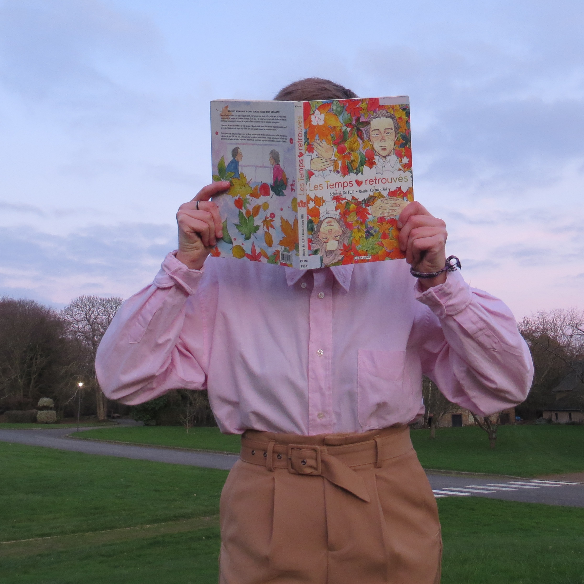 personne en chemise rose lisant Les Temps Retrouvés de Kei Fujii & Cocoro Hirai devant un coucher de soleil
