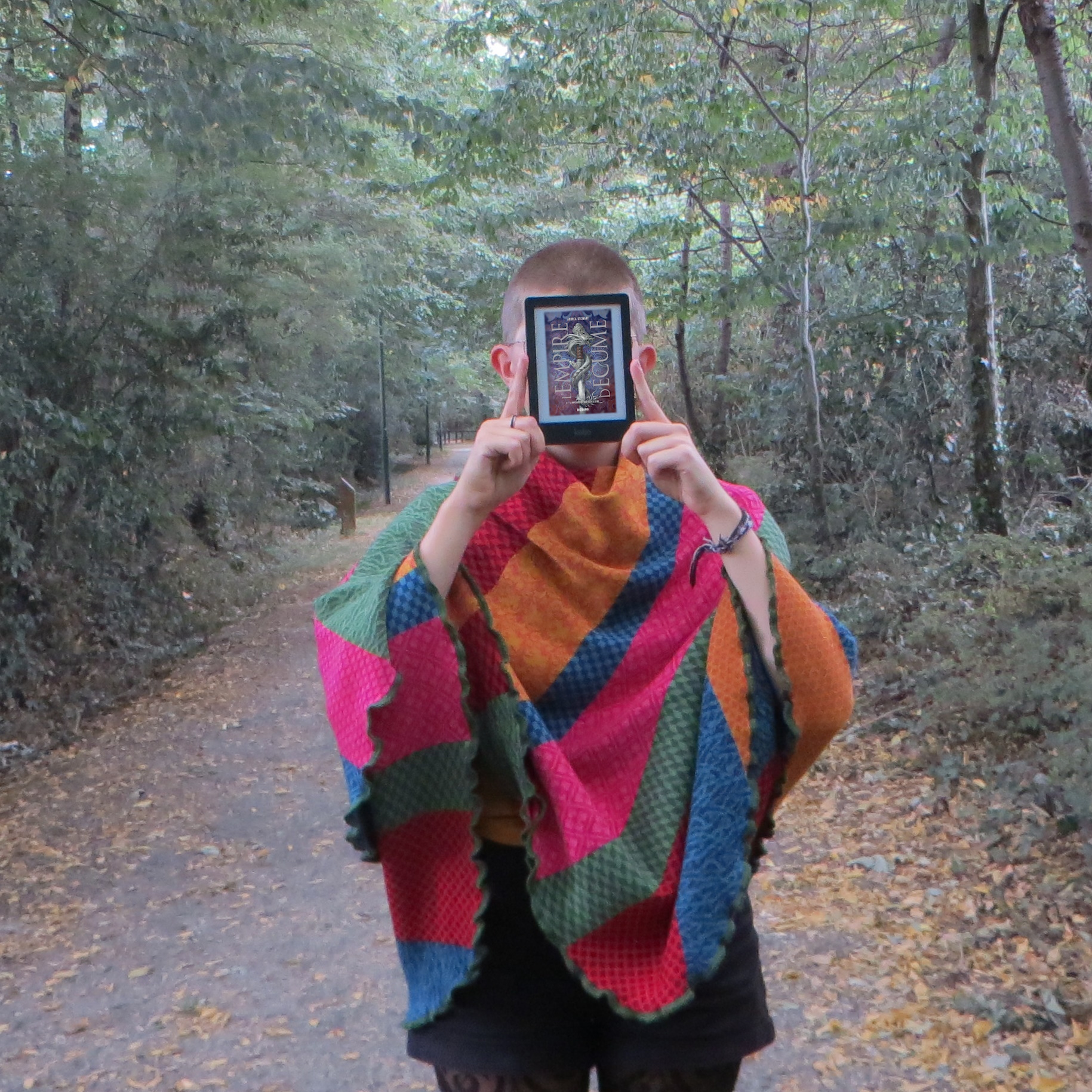 personne portant un gilet multicolore lisant L’Empire d’Écume tome 3 : The Bone Shard War de Andrea Stewart dans la forêt