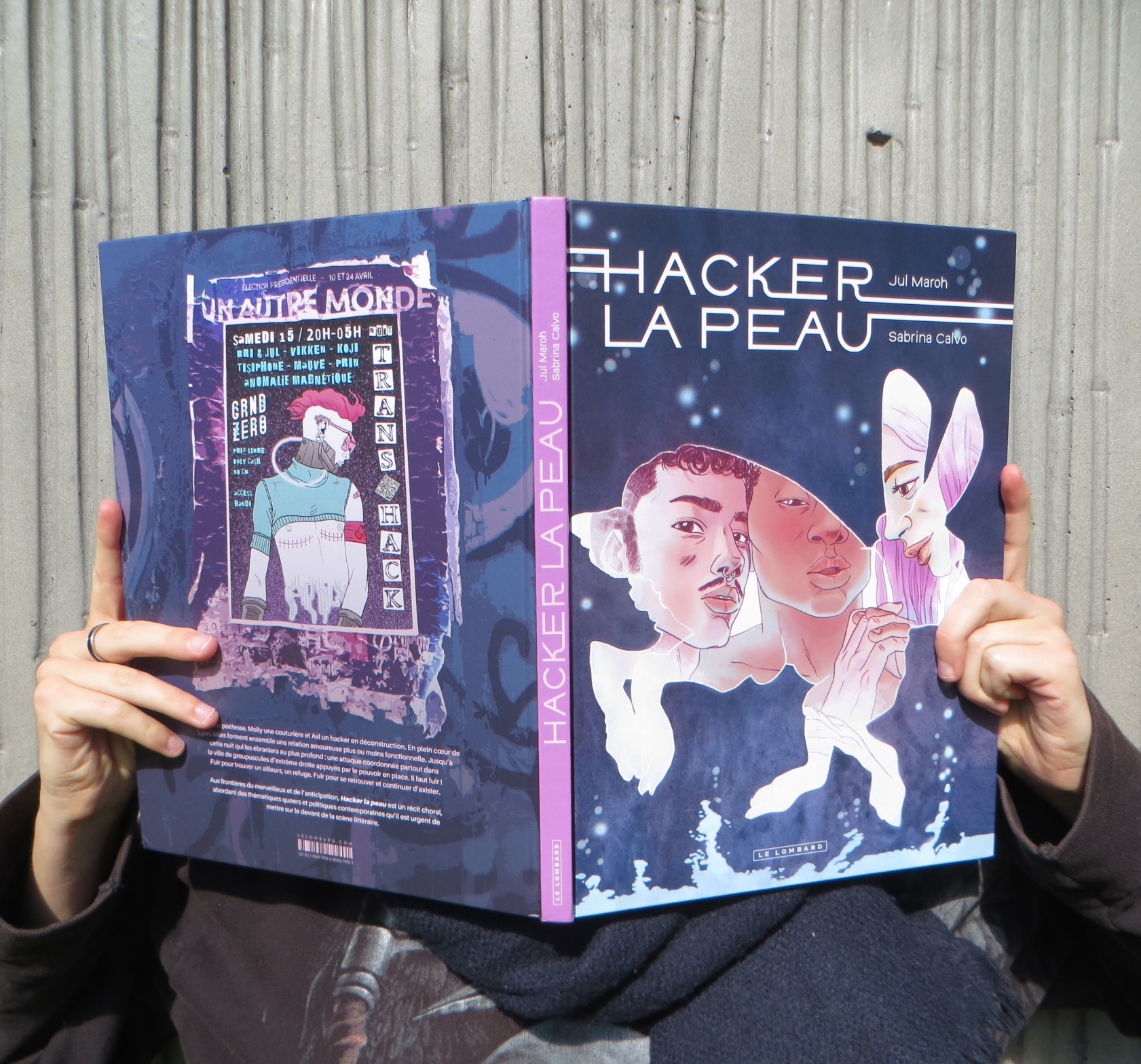 personne en pull sombre lisant Hacker la Peau de Sabrina Calvo et Jul’ Maroh devant un mur gris strié