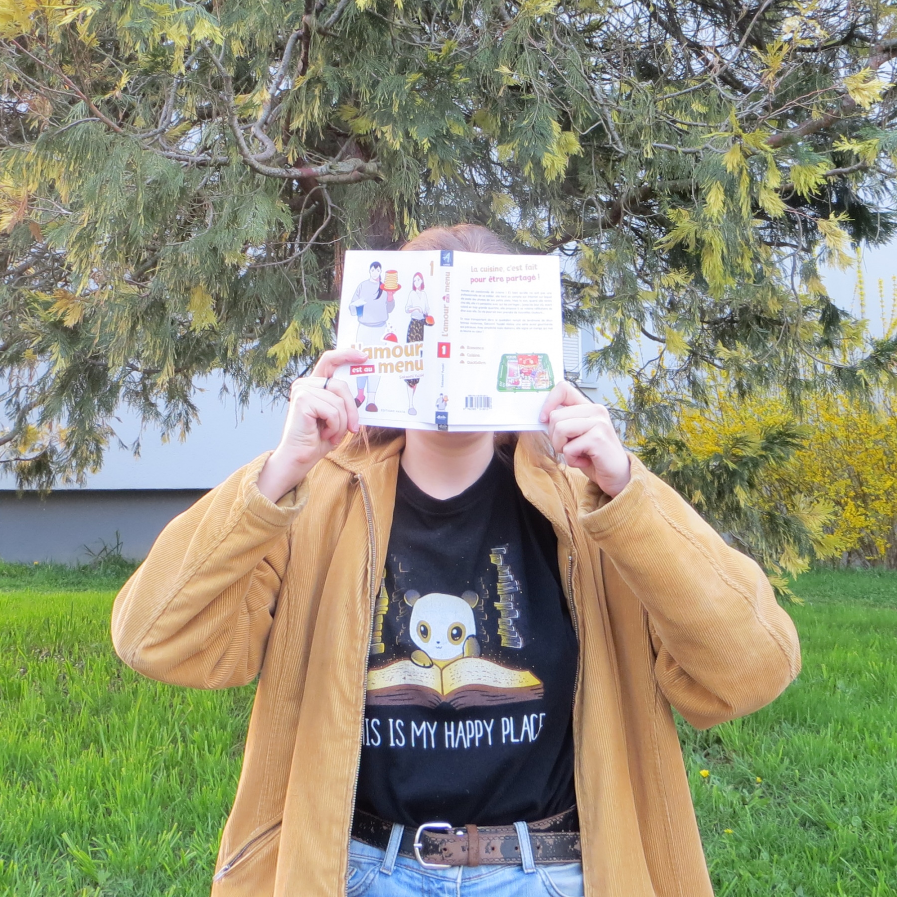 personne en veste jaune lisant L’amour est au Menu de Sakaomi Yuzaki devant un arbre en fleur