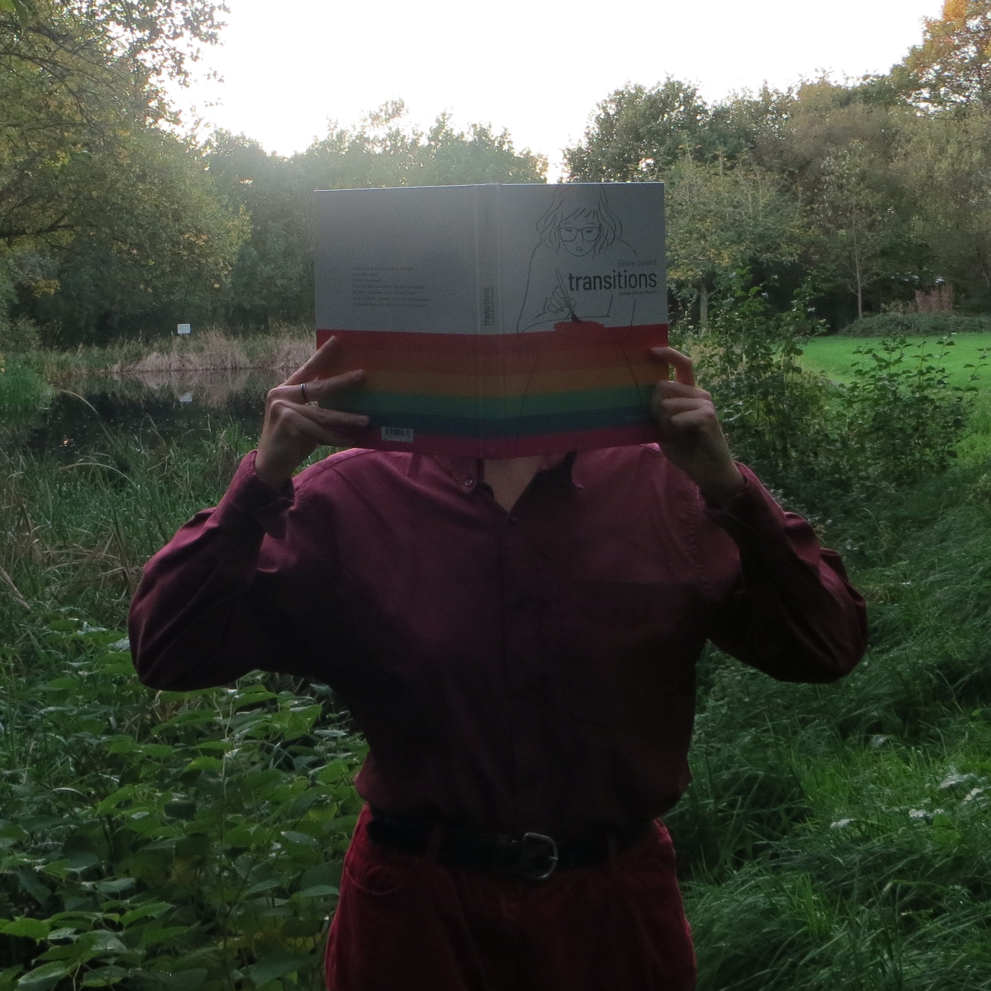 personne en tenue rouge lisant Transitions - Journal d'Anne Marbot de Elodie Durand devant un étang