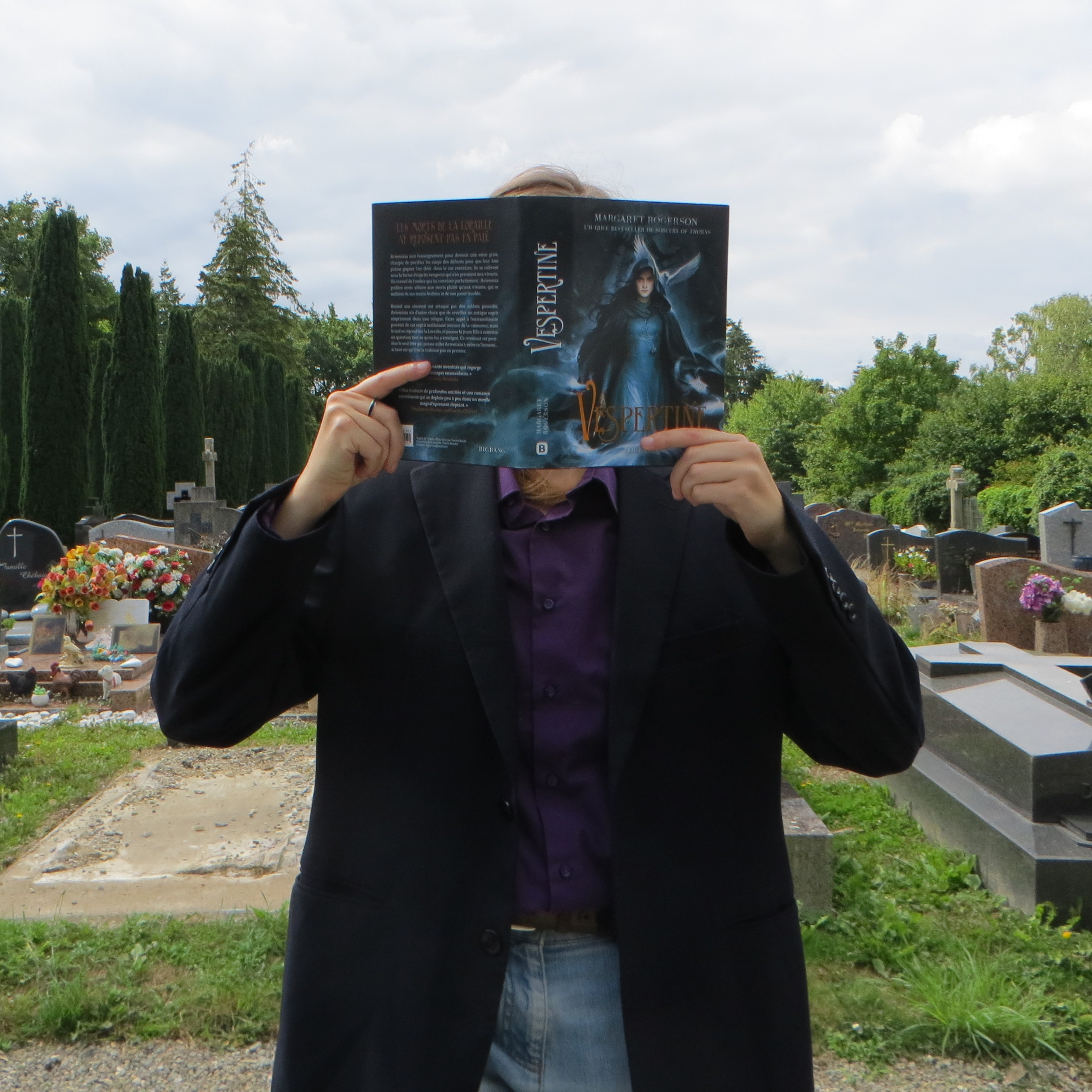 personne en chemise sombre lisant Vespertine de Margaret Rogerson dans un cimetière